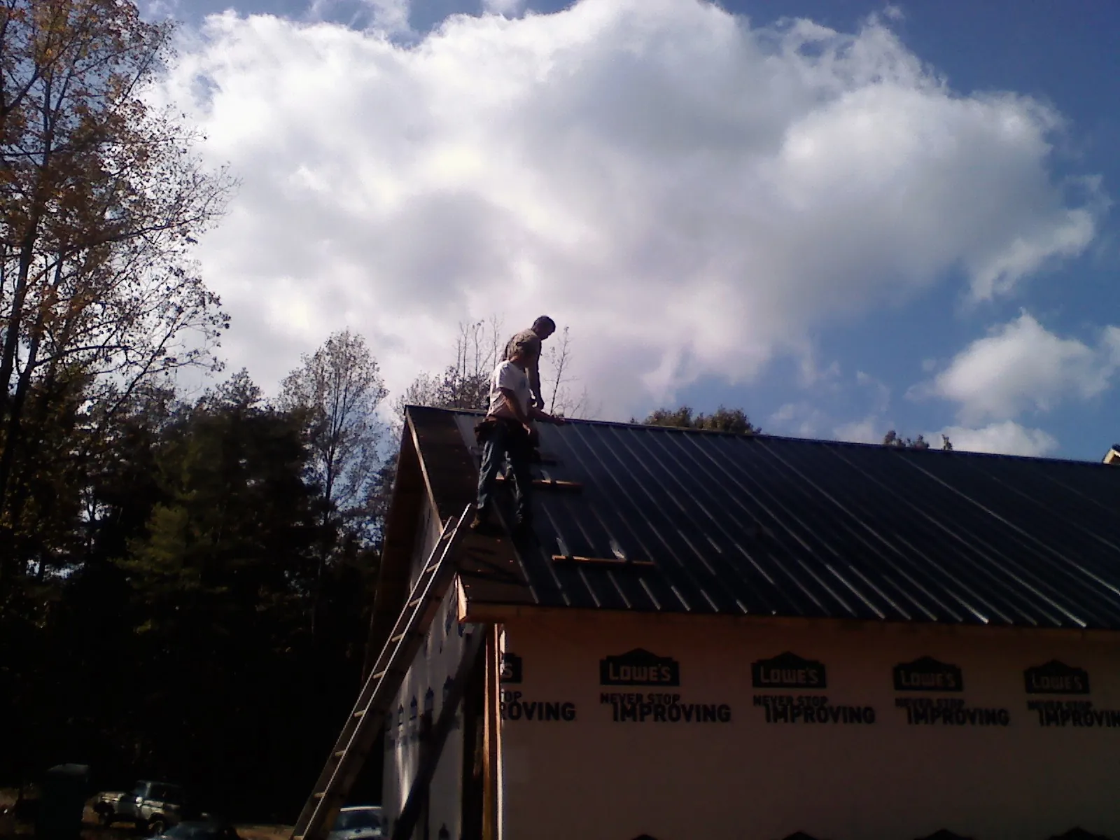 Roofer fastening dark metal panels high against a cloudy sky, from a Roof Inspection job in Woodburn