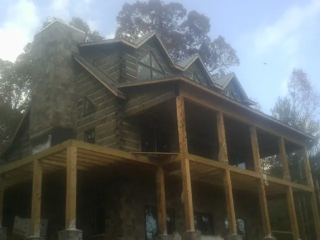 Stone chimney and dormers on a large log home with a timber porch in Woodburn