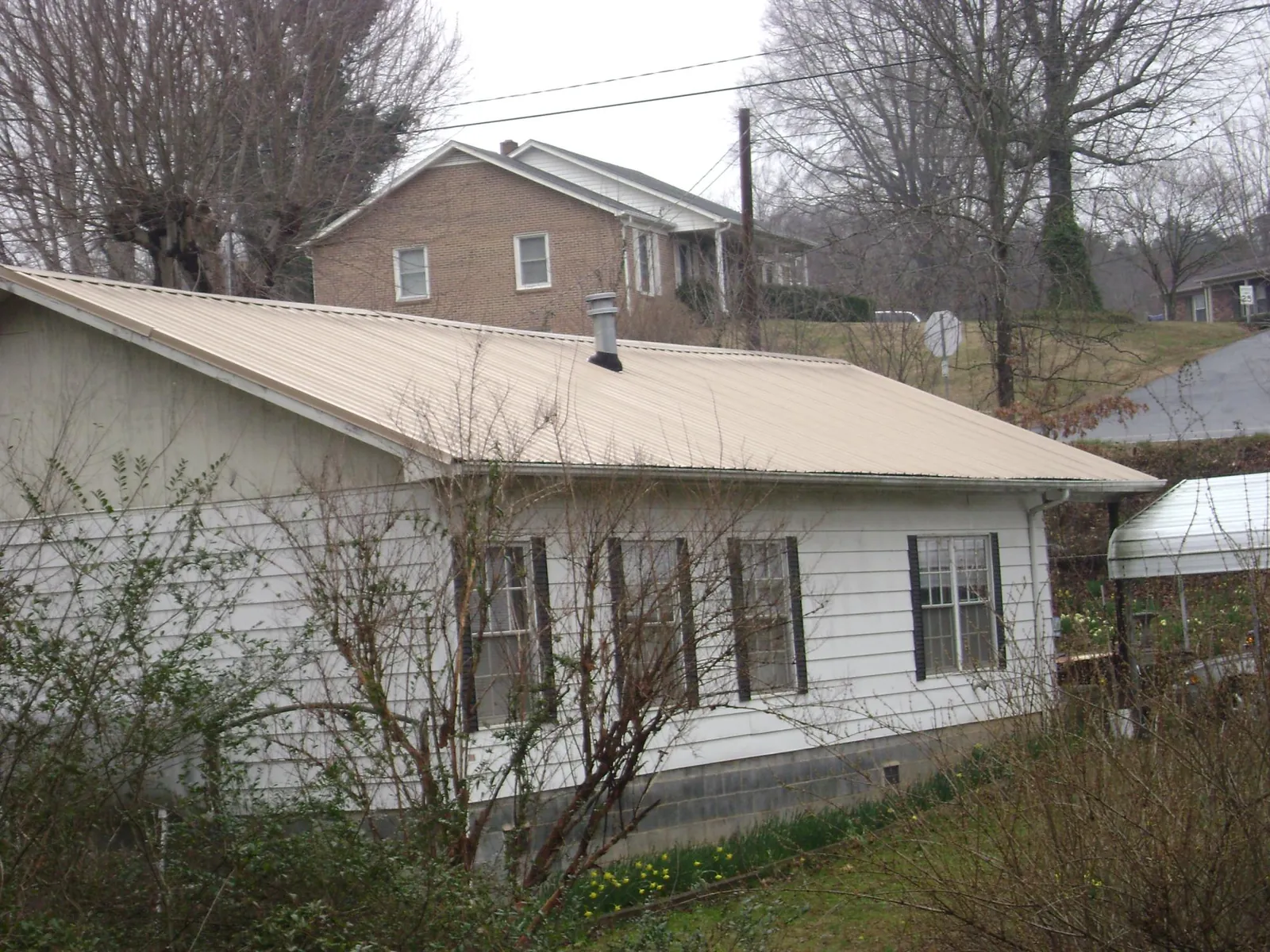 Tan metal roof on a white sided house set into a hillside — Commercial Roofing by Roofing Brothers in Woodburn